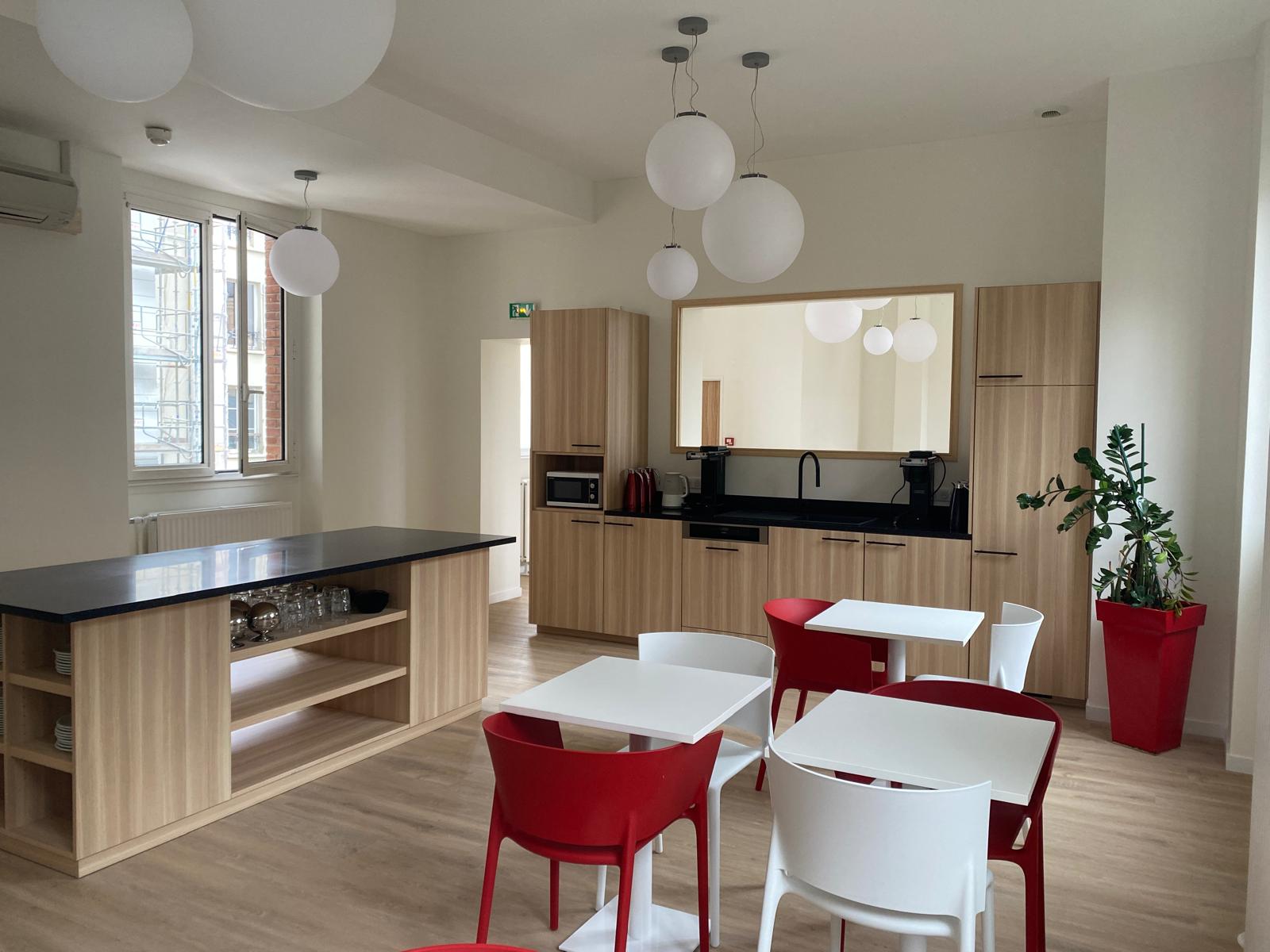 Espace de restauration rénové avec kitchenette bois, plan noir et mobilier rouge et blanc